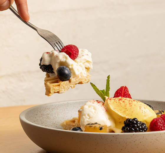 A close up perspective of a fork grabbing a bite from the delicious waffles topped with ice cream and fresh berries.