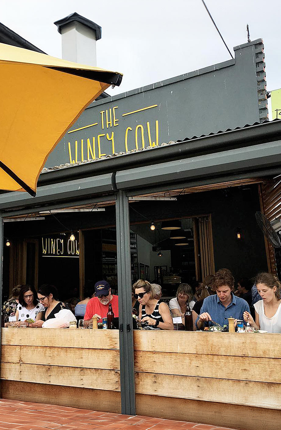 The outside of the Mornington location with people sitting and eating on the bar seating that overlooks the boardwalk.