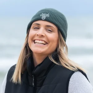 A young woman wearing a green beanie with The Winey Cow logo in white on the front.