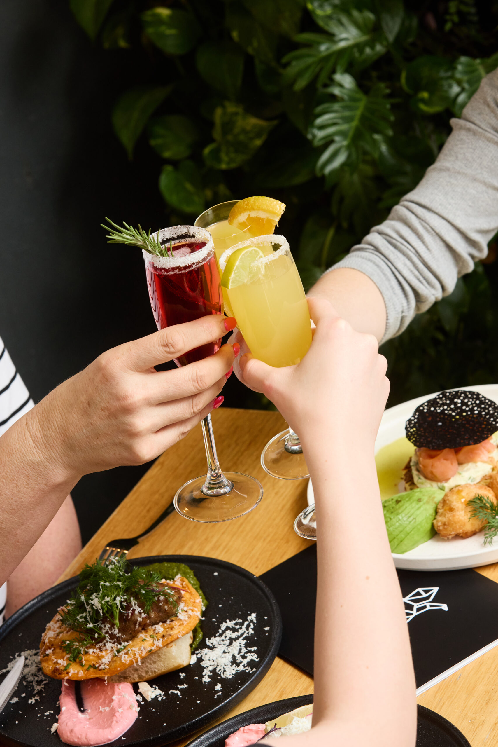 Guests toasting with vibrant mimosas during Boozy Brunch at The Winey Cow, surrounded by colourful brunch dishes and a lively, relaxed atmosphere.