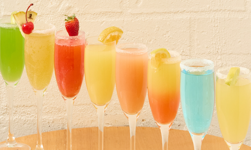 A colourful lineup of premium mimosas from The Winey Cow's Boozy Brunch menu, featuring a variety of vibrant flavours garnished with fresh fruit and served in sugar-rimmed champagne flutes