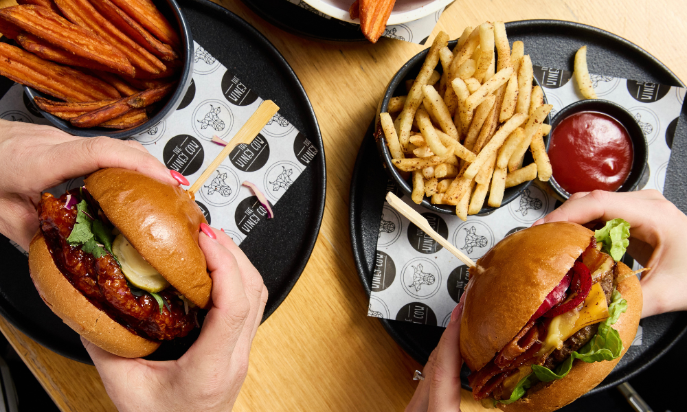 Two burgers being shown to the camera with hands holding them